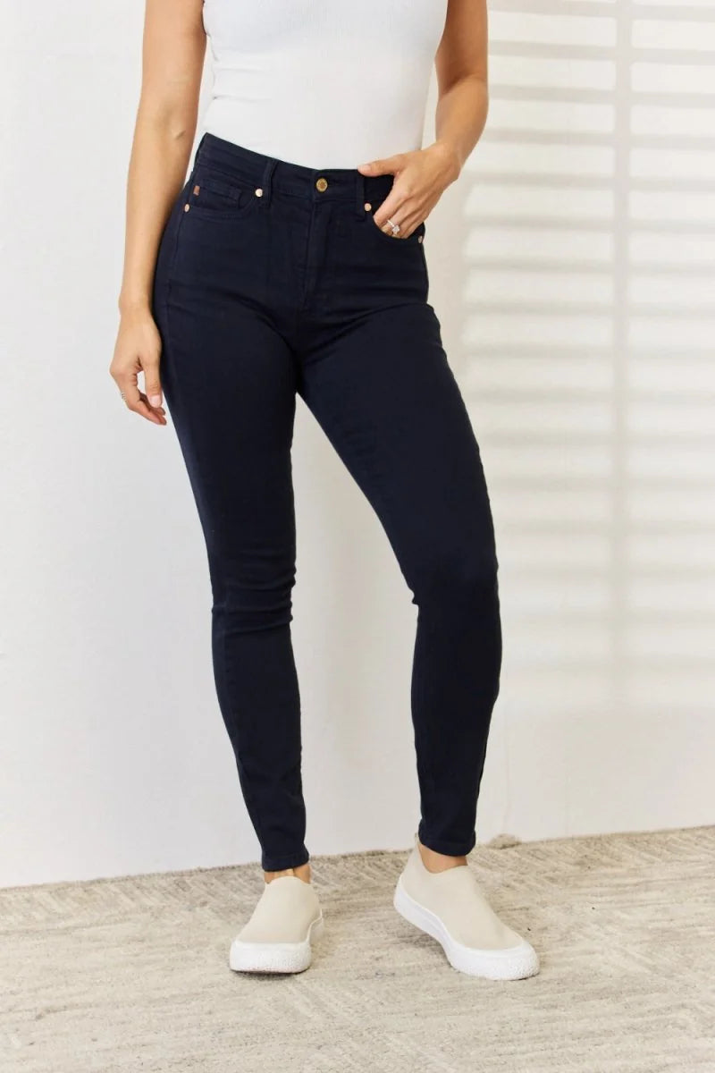 Navy blue skinny jeans with gold button detail on a model wearing white sneakers.