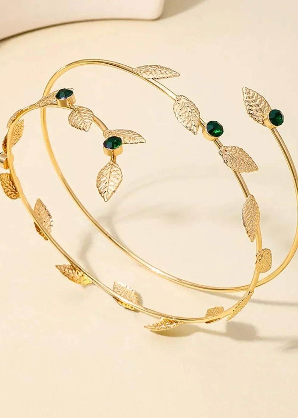 Gold-plated arm cuff with leaf details and green rhinestones, open design.