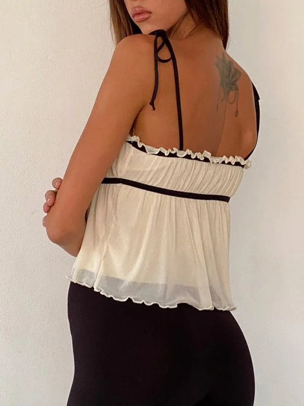 Sheer, cream-colored cami with black trim and tie straps, tucked into black leggings.