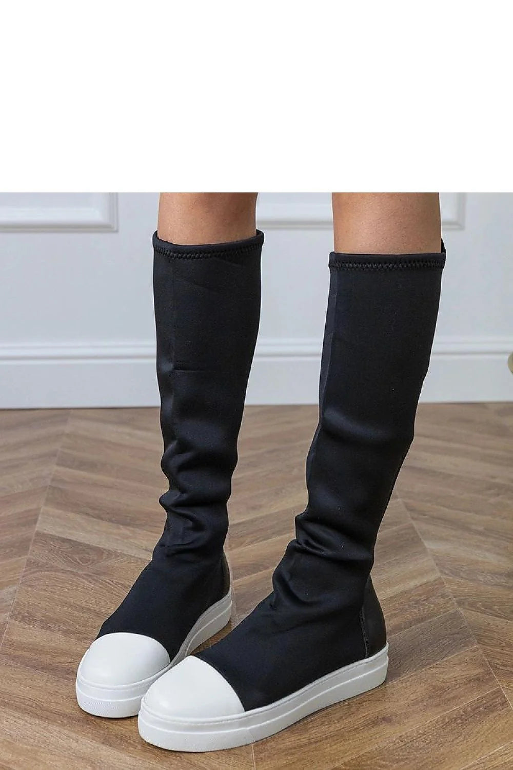 Black knee-high boots with white toe caps and platform soles, worn by a model.