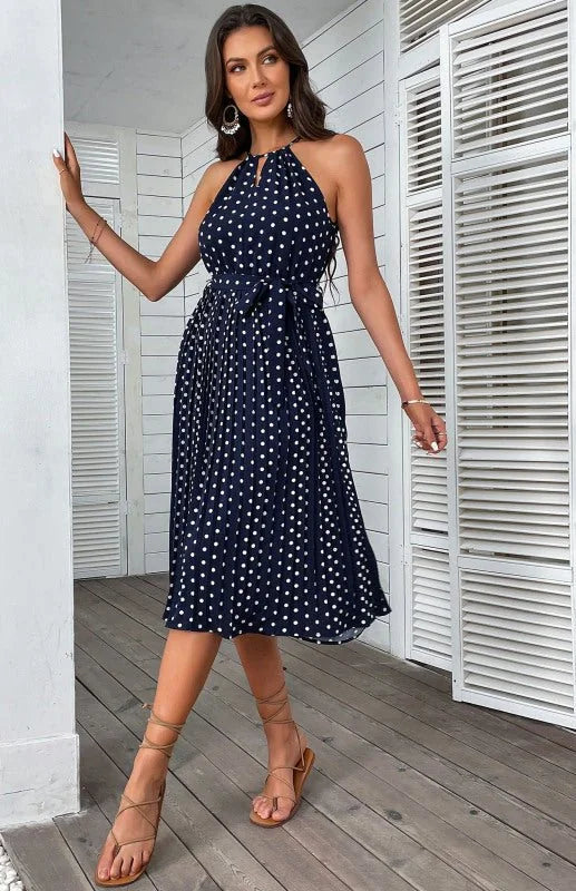 Navy blue polka dot halter dress with tie waist and pleated skirt, worn by a model.
