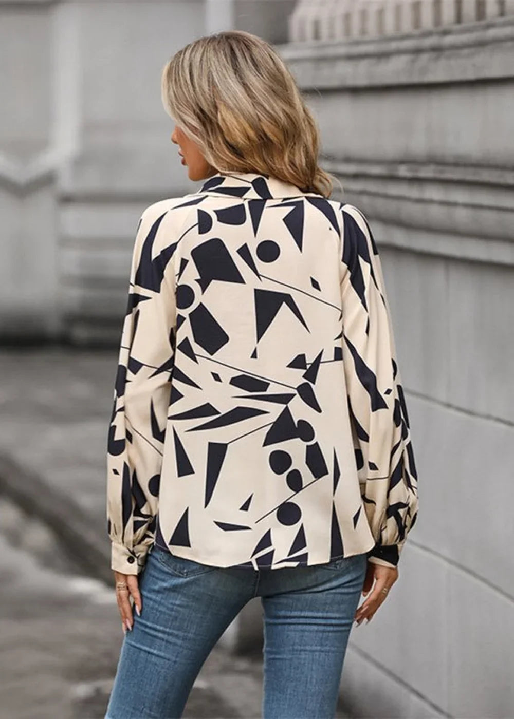 Back view of a cream blouse with a black abstract geometric print, long sleeves, and a collared neckline.