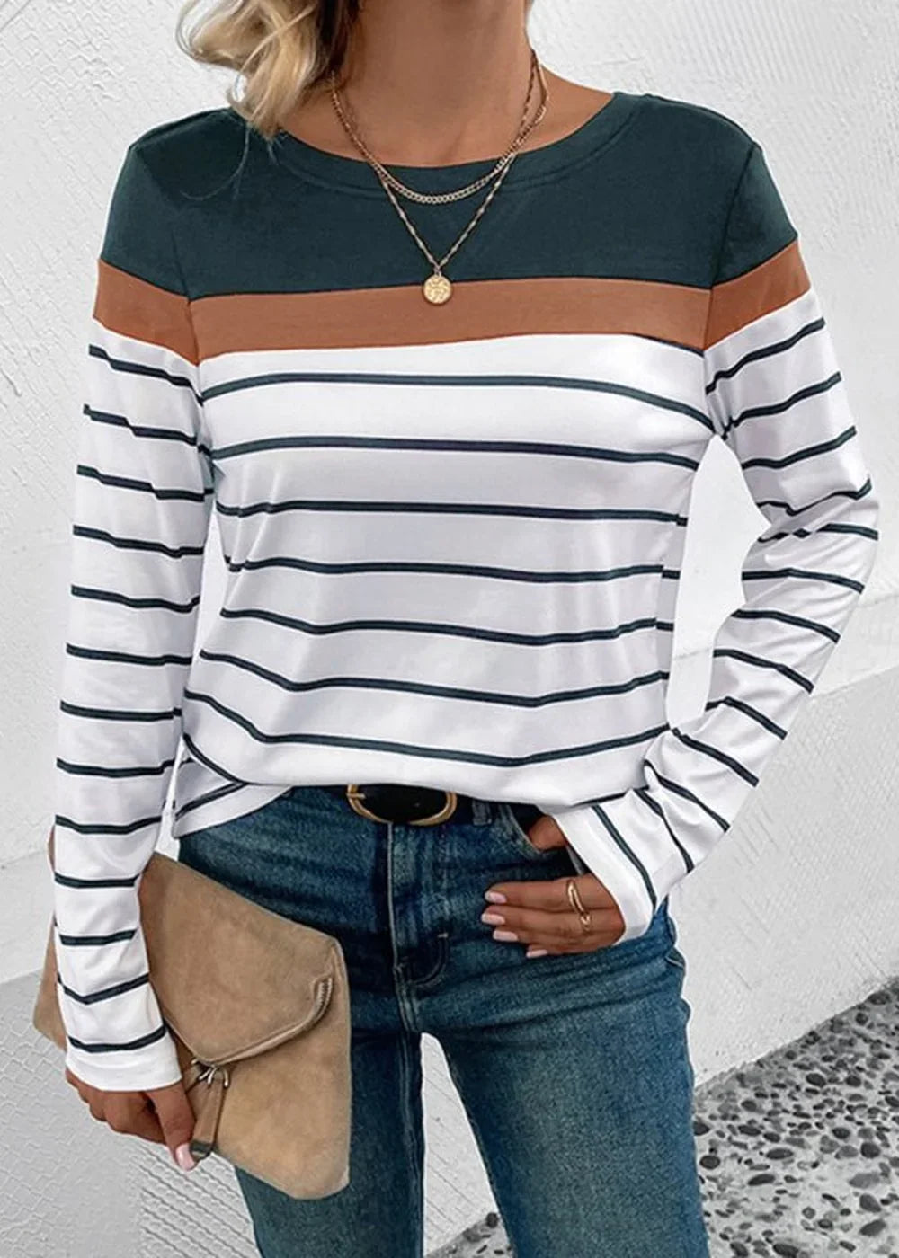 Long-sleeve striped top with green, brown, and white bands, worn with blue jeans and a tan clutch.