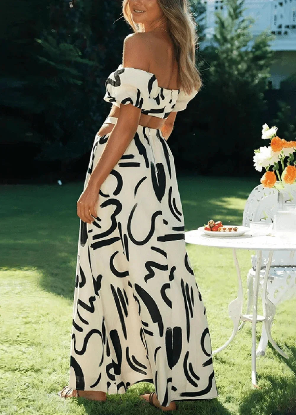 Off-the-shoulder white crop top and flowing maxi skirt with a bold black abstract print, worn by a model outdoors.