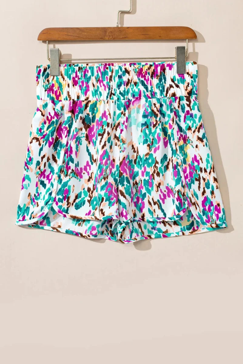 White shorts with a colorful abstract print in pink, teal, and brown, featuring a gathered elastic waistband.