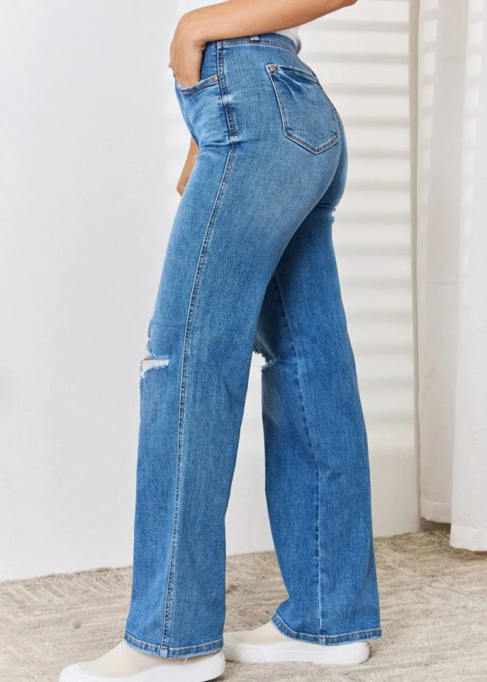 Medium wash distressed wide-leg jeans on a model, showing a ripped knee and the flared hem.