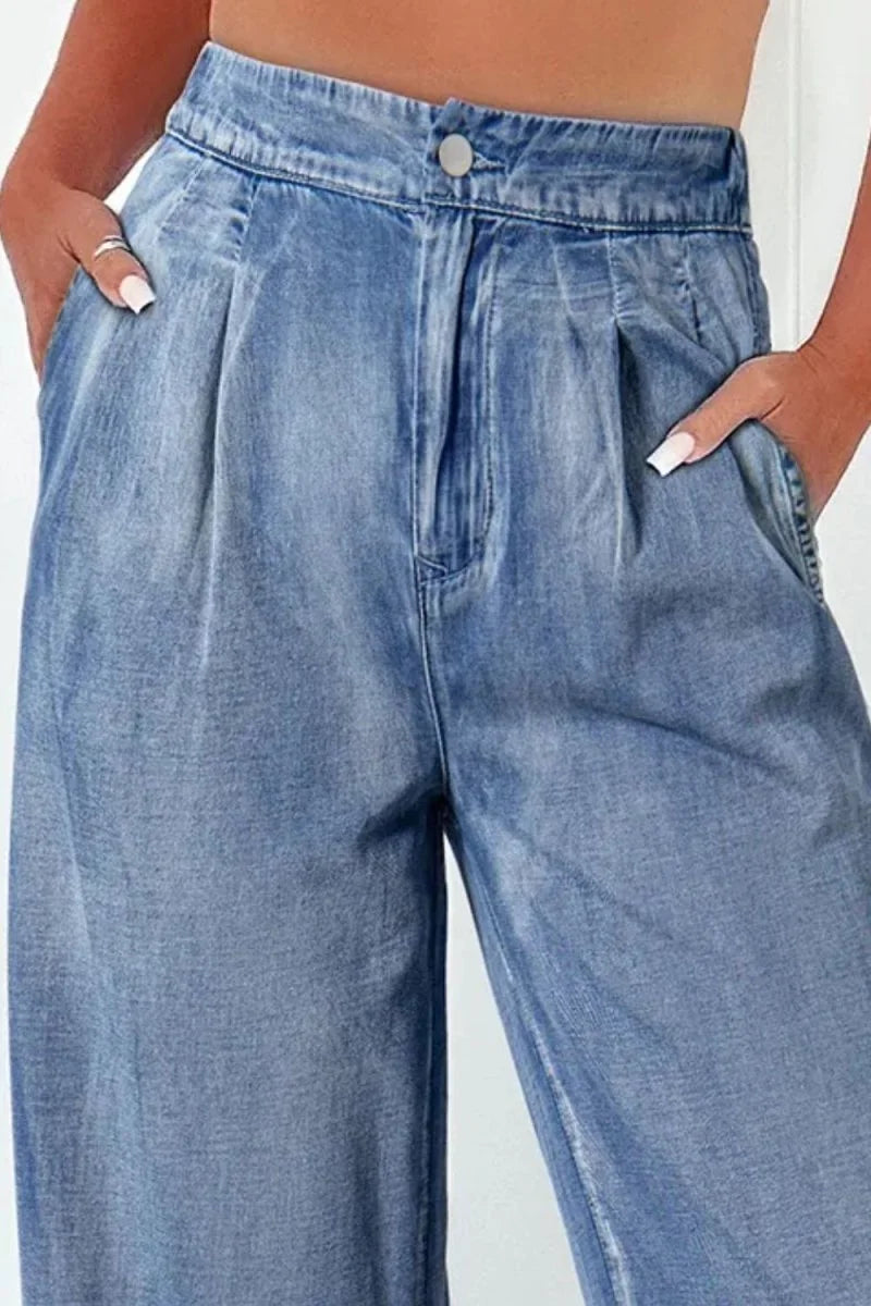 Light wash denim pants with pleats and a button closure, showing texture and pockets.