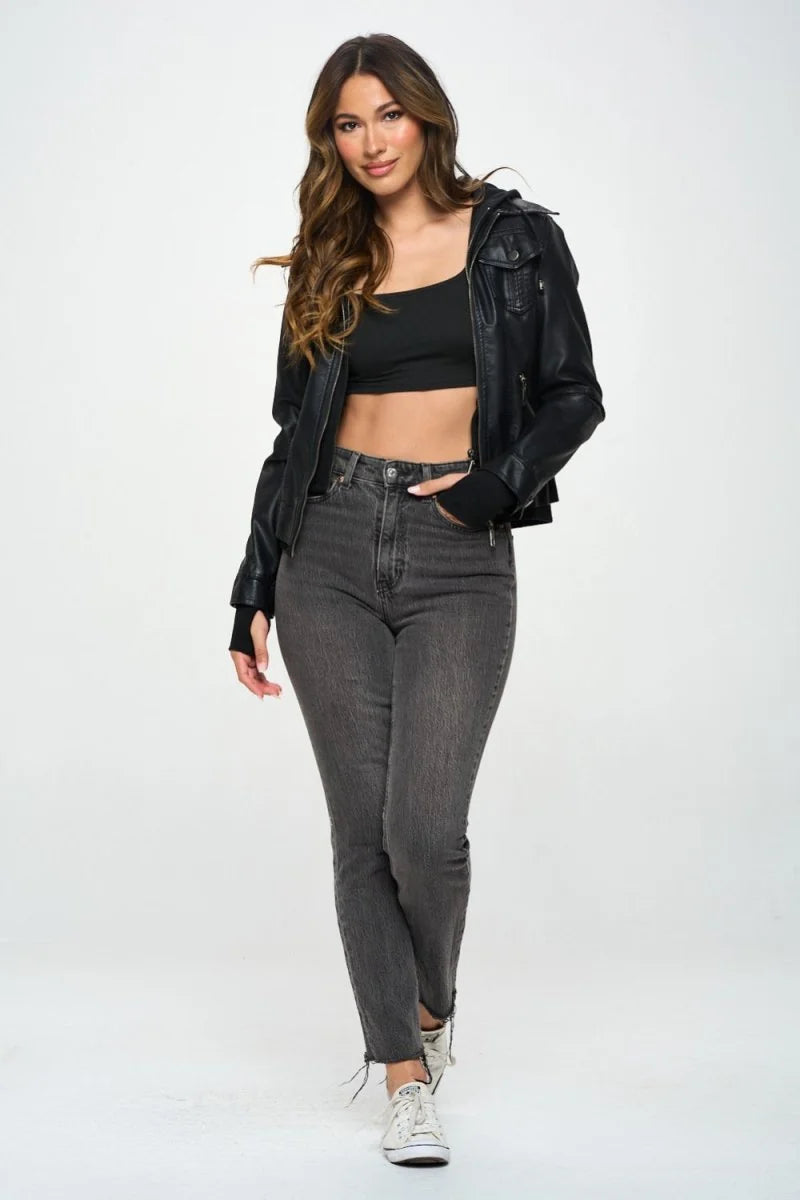 Black vegan leather moto jacket with a cropped fit, worn by a model in gray jeans and white sneakers.