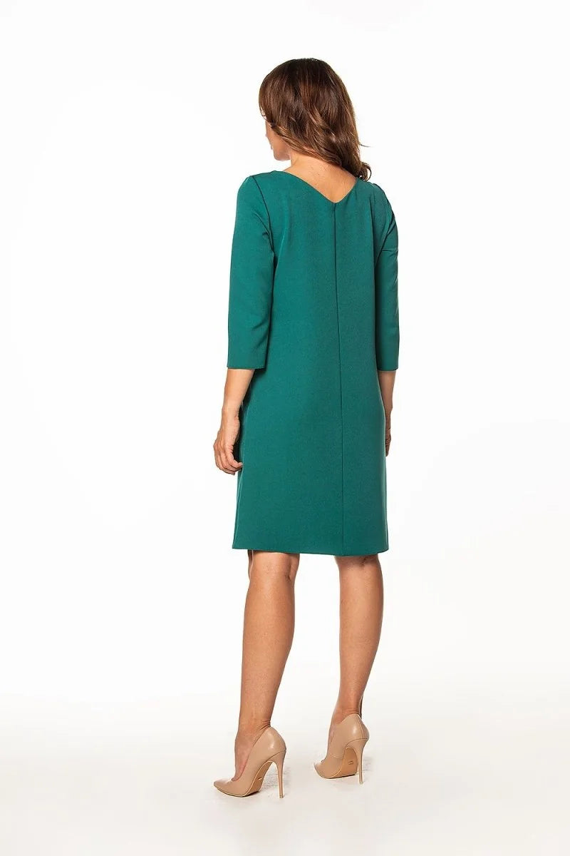 Back view of a woman wearing a knee-length teal dress with three-quarter sleeves and nude high heels.
