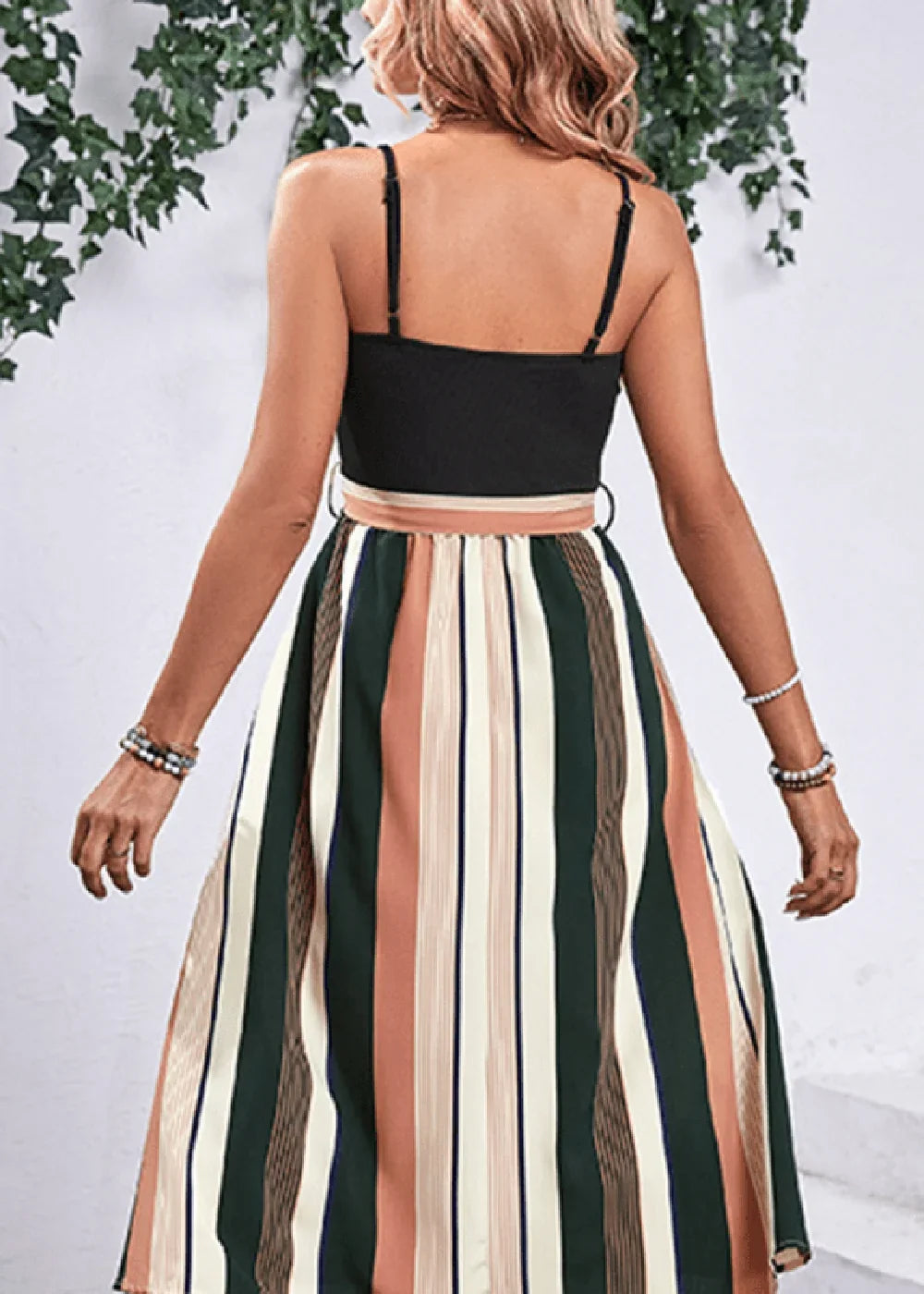 Back view of a woman wearing a black cami top with a flattering striped maxi skirt in green, peach, and cream.