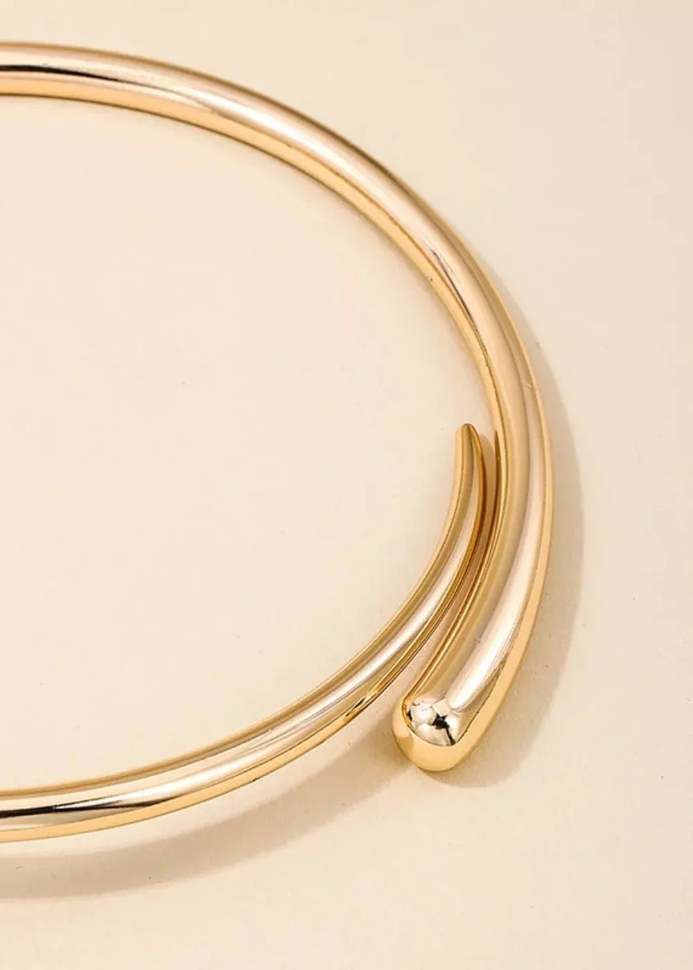 Close-up of a shiny gold-plated collar necklace with a sleek, open design.