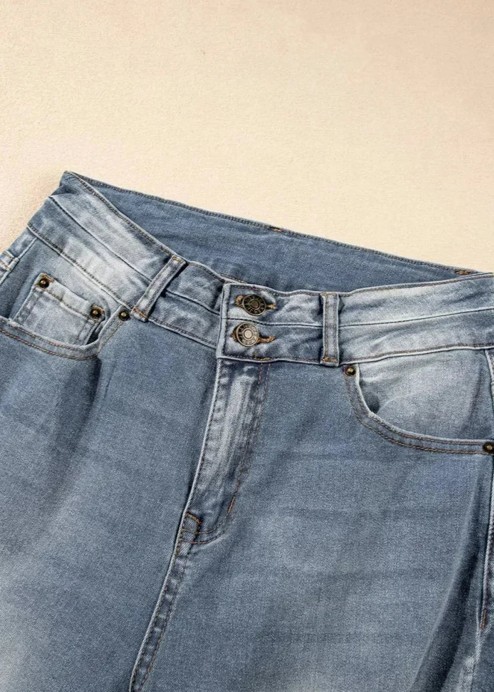 Close-up of high-rise light wash denim jeans with double button closure and pocket details.