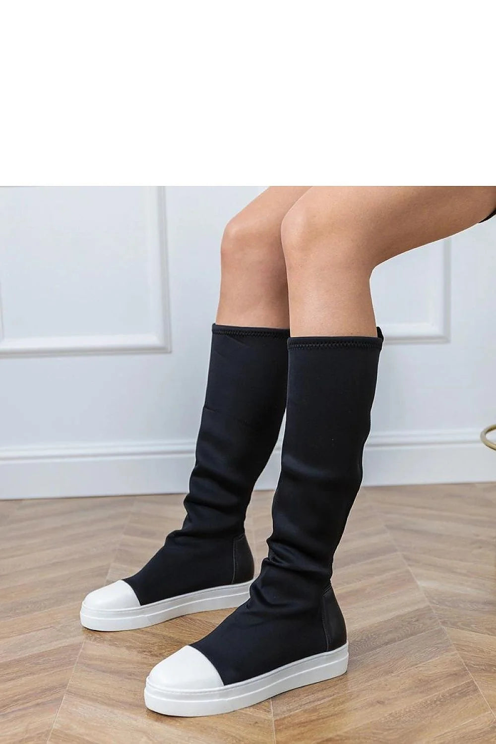 Black knee-high boots with white toe caps and white soles on a wooden floor.