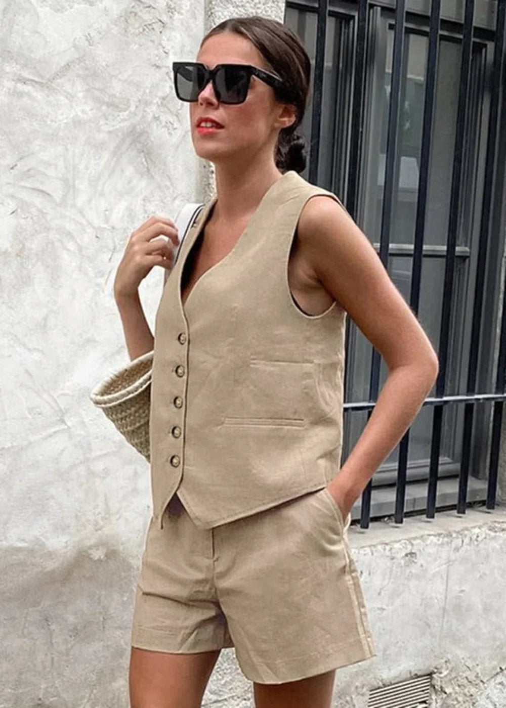 Model wears a beige linen vest and shorts set with a straw bag.