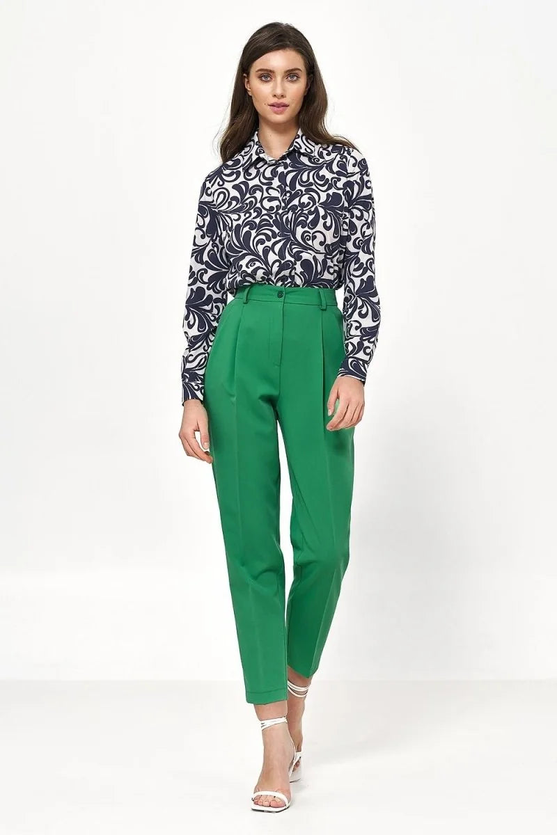 Emerald green high-waisted trousers with pleats and a tapered leg, on model.