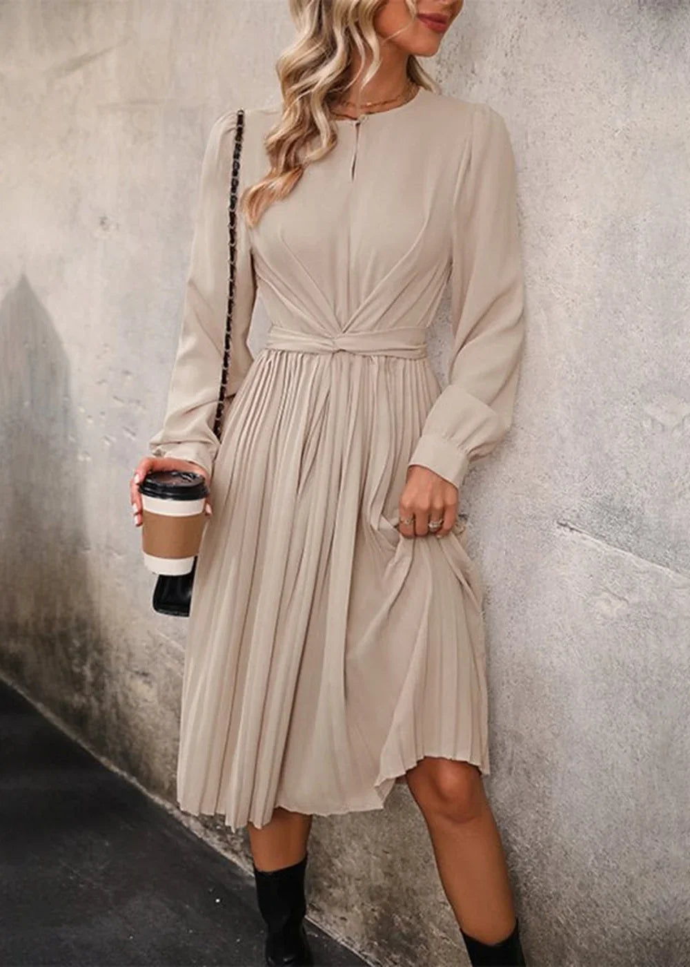 Beige pleated midi dress with ruched waist detail, worn by a model holding a coffee cup.