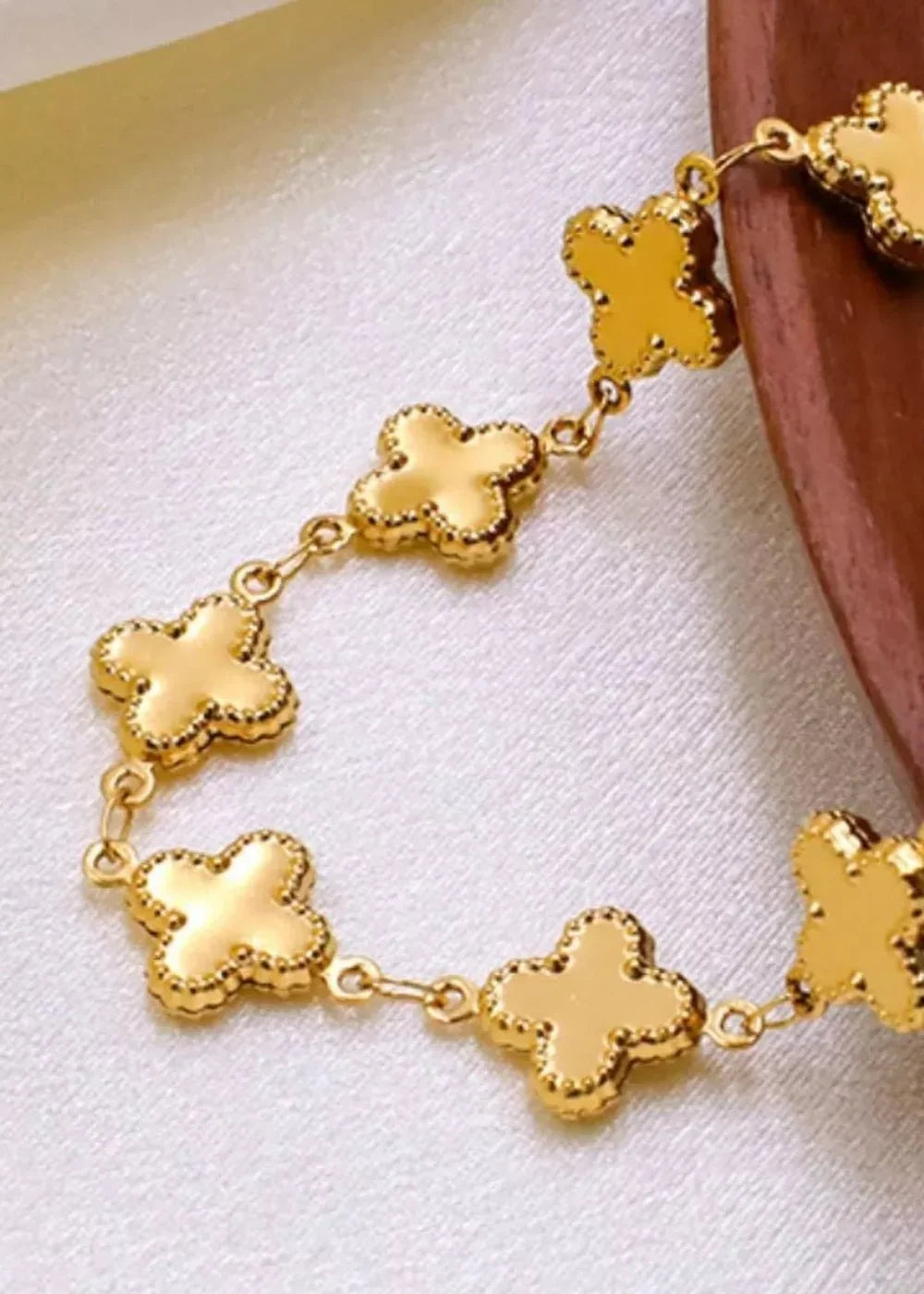 Close-up of a gold-plated clover-shaped bracelet with a textured edge on a satin-like surface.