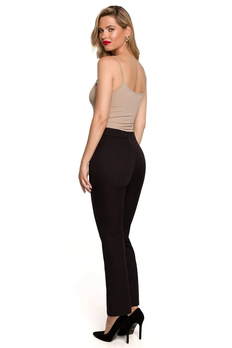 Woman in black high-waisted pants and beige camisole, showing back view.