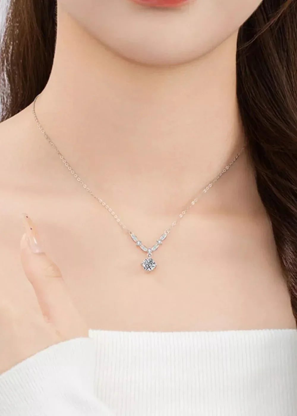 Close-up of a delicate silver chain necklace with a sparkling Moissanite pendant on a woman's neck.