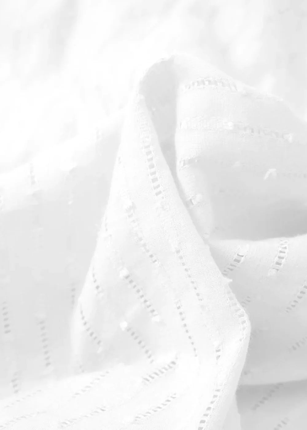 Close-up of white cotton fabric with embroidered eyelet details and a textured weave.