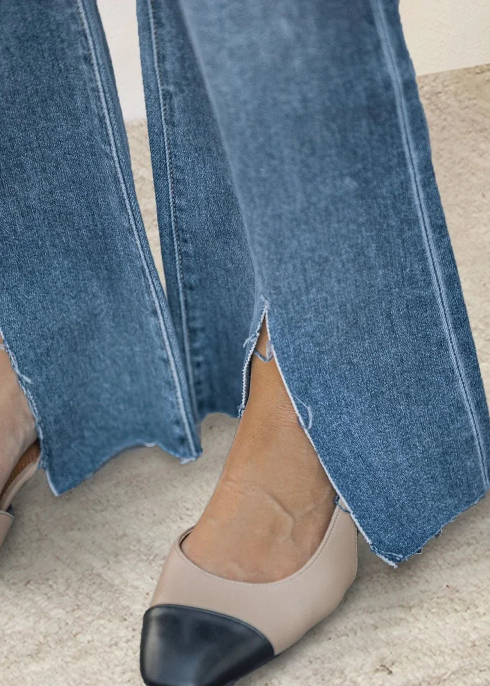 Close-up of medium wash denim jeans with frayed, split hems and two-tone cap-toe flats.
