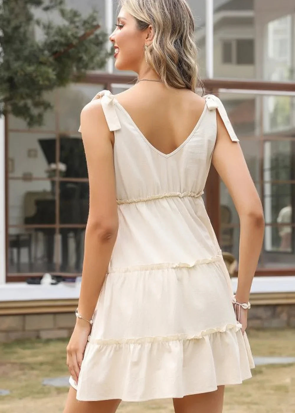 Cream tiered mini dress with v-neck and tie straps, showing back view on model.