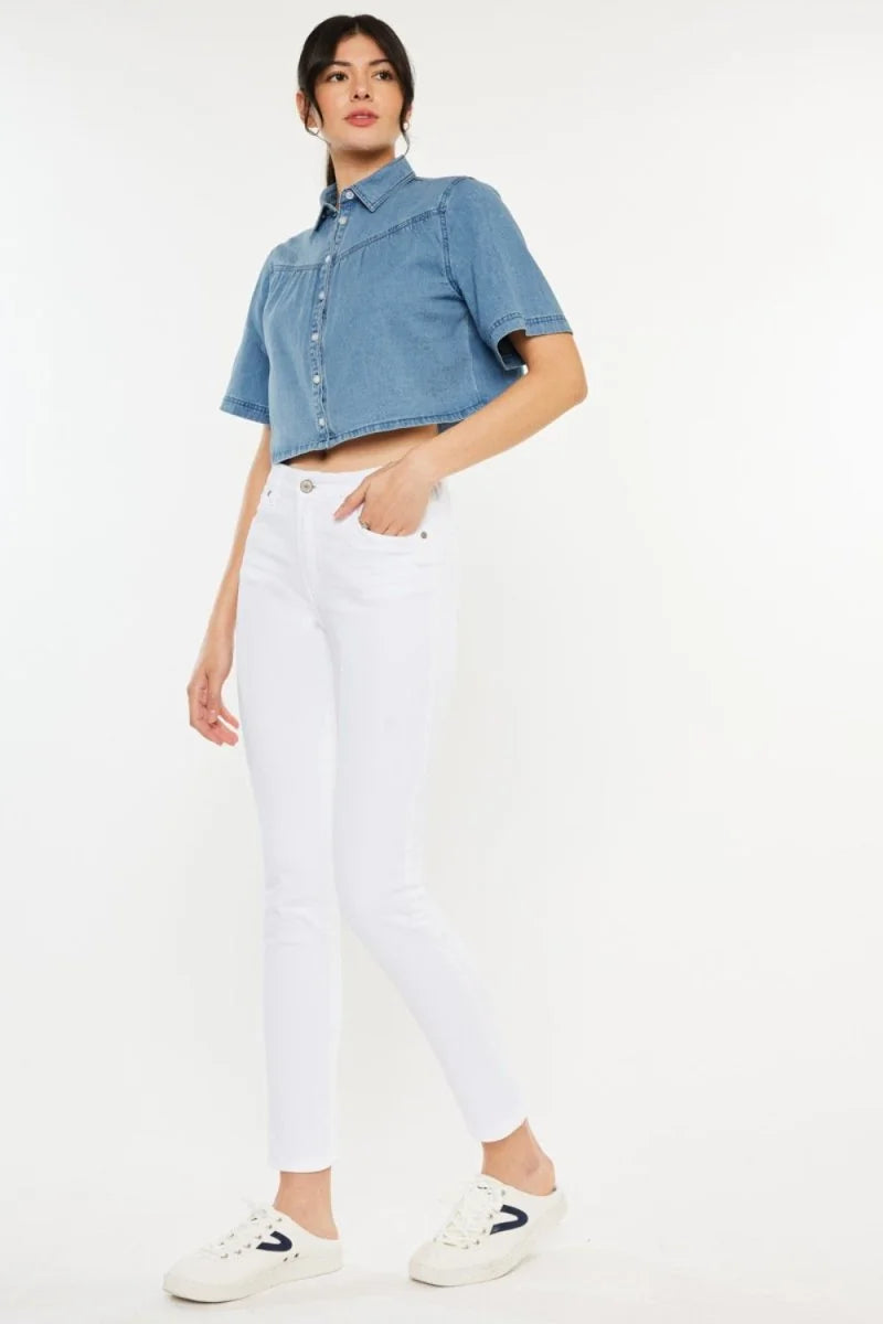 Woman in white slim-fit jeans and a cropped denim shirt, standing against a white background.