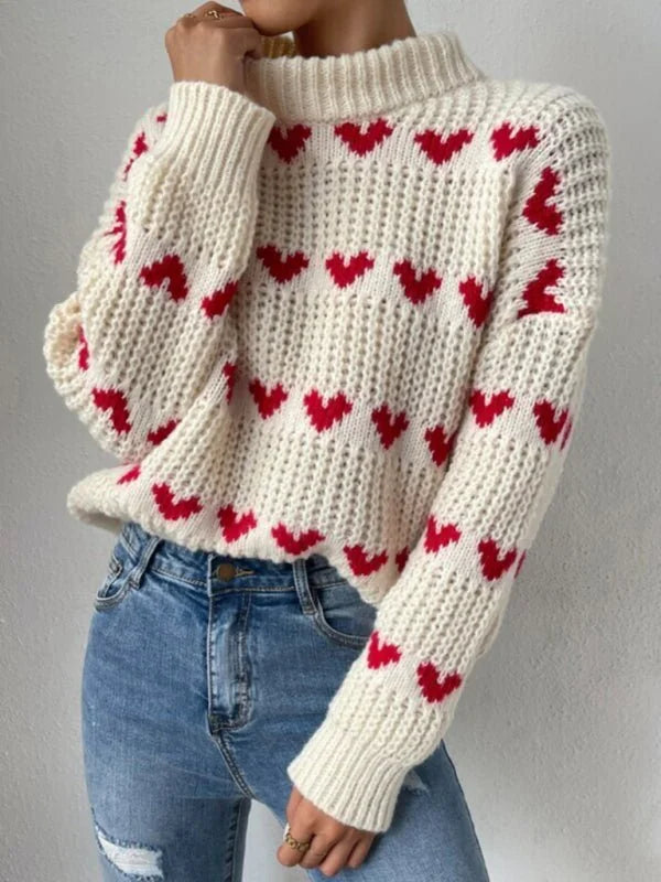 Cream knit sweater with red hearts pattern and blue denim jeans on model.