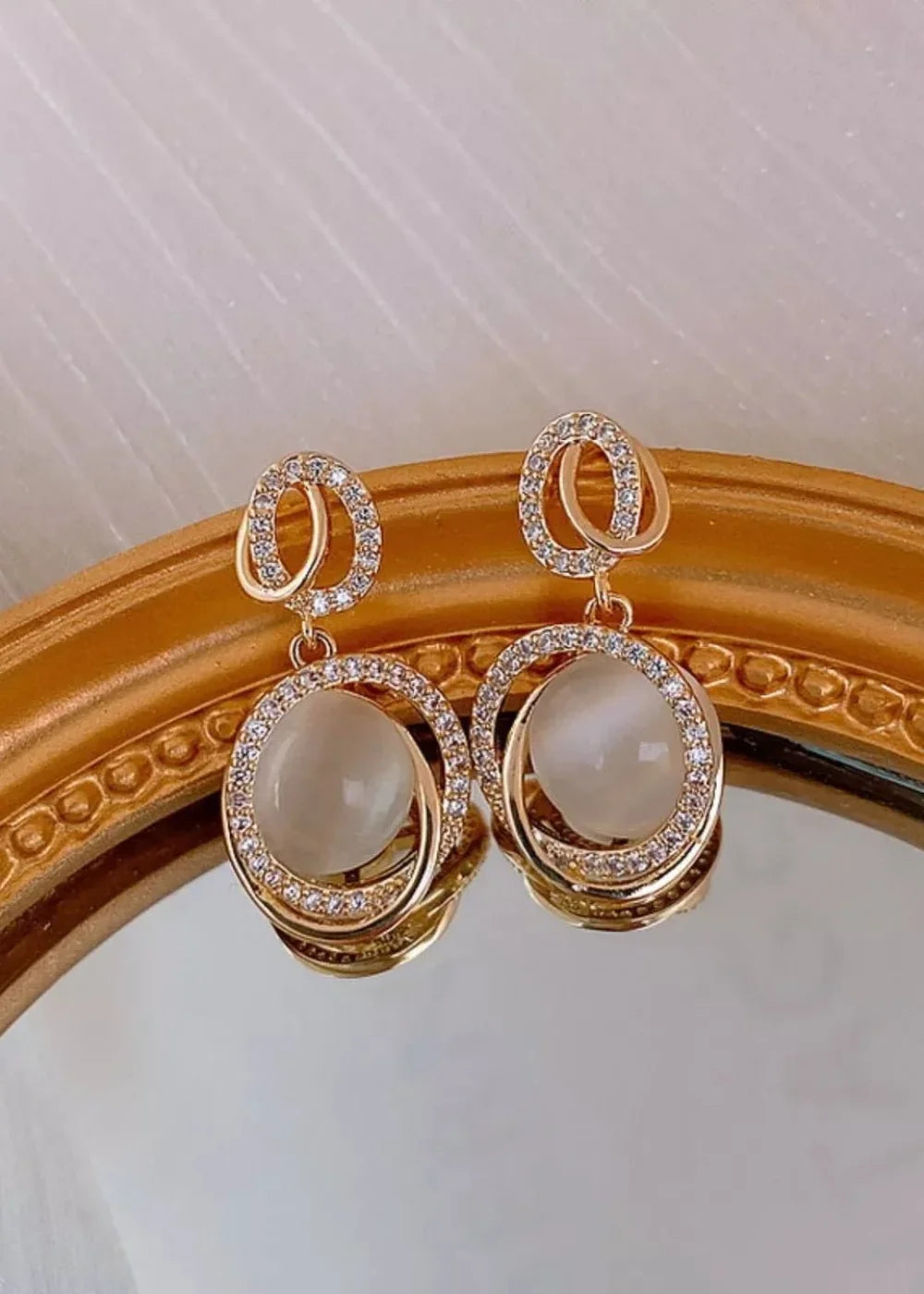 Gold-plated earrings with oval cat's eye stones and diamond-like accents.