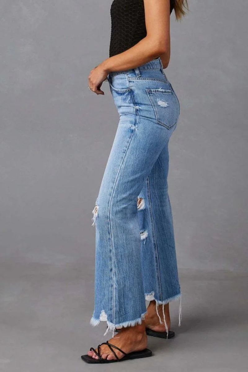 Distressed light wash denim jeans with a frayed hem and wide leg fit.