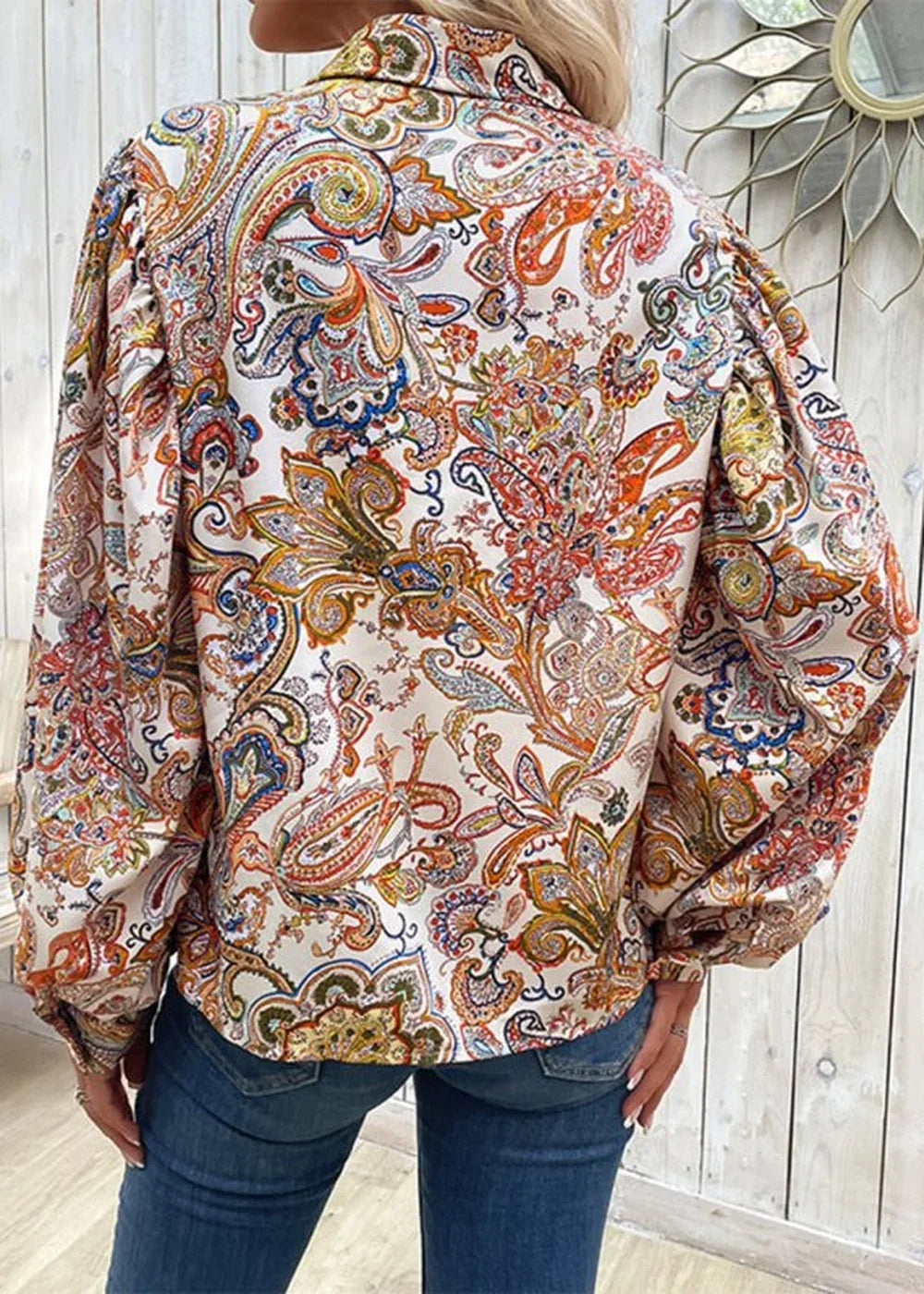 Back view of a white blouse with a colorful paisley print and puff sleeves.