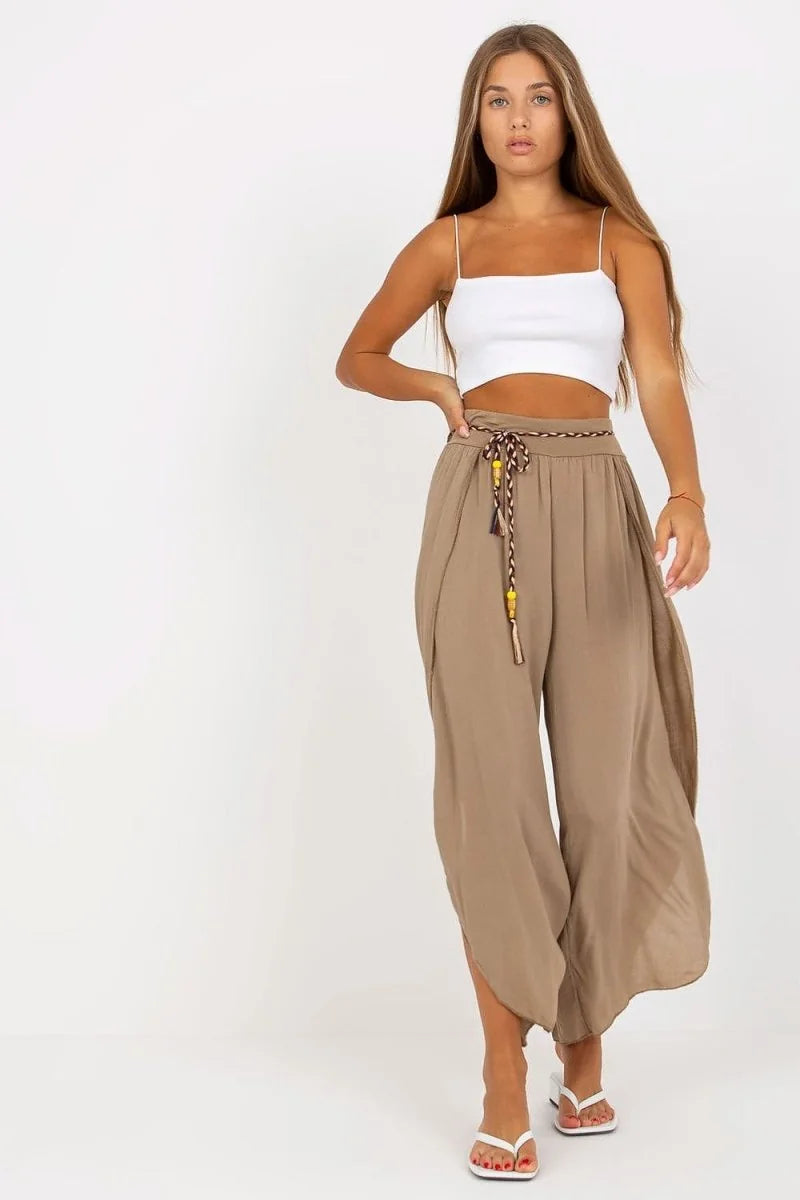 Model in flowy, taupe viscose palazzo pants with a braided tassel belt.
