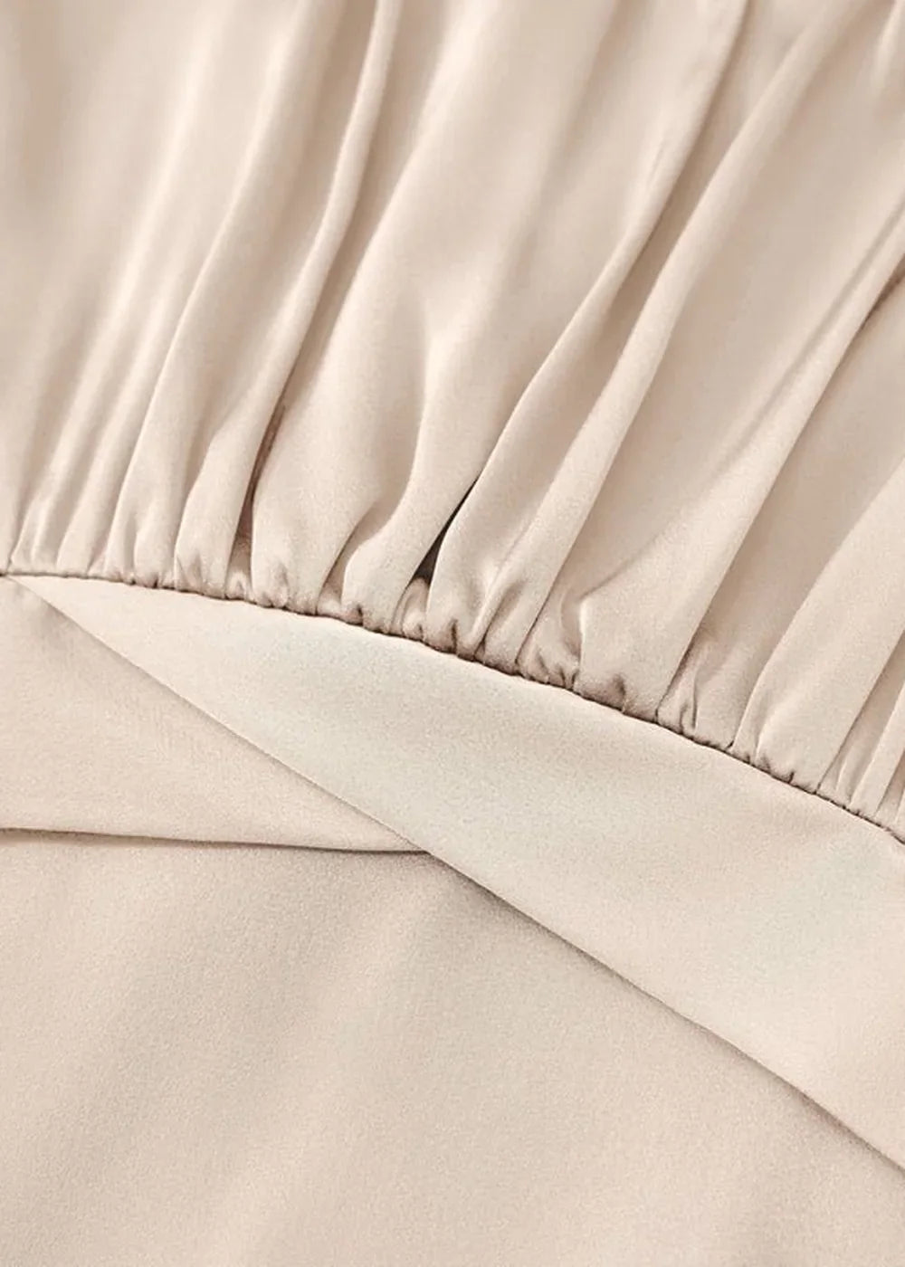 Close-up of a beige polyester jumpsuit showing gathered fabric texture and a smooth overlay.