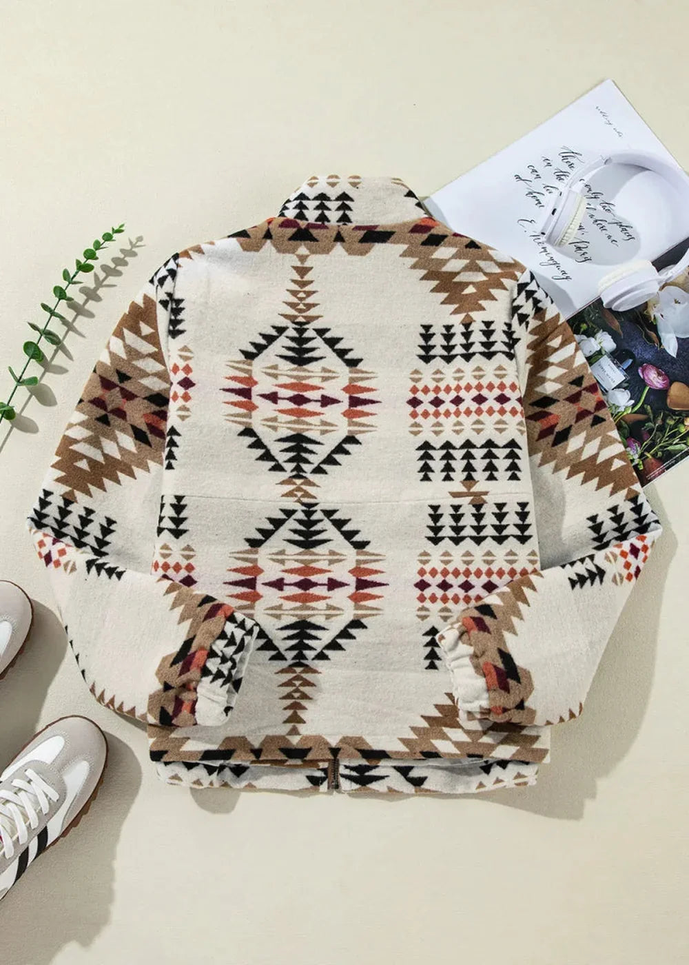 Cream jacket with a geometric Aztec-inspired pattern in brown, black, and rust red, featuring a zip-up front.