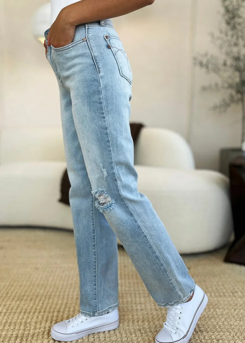Light wash distressed denim jeans with frayed knee detail, worn with white sneakers.
