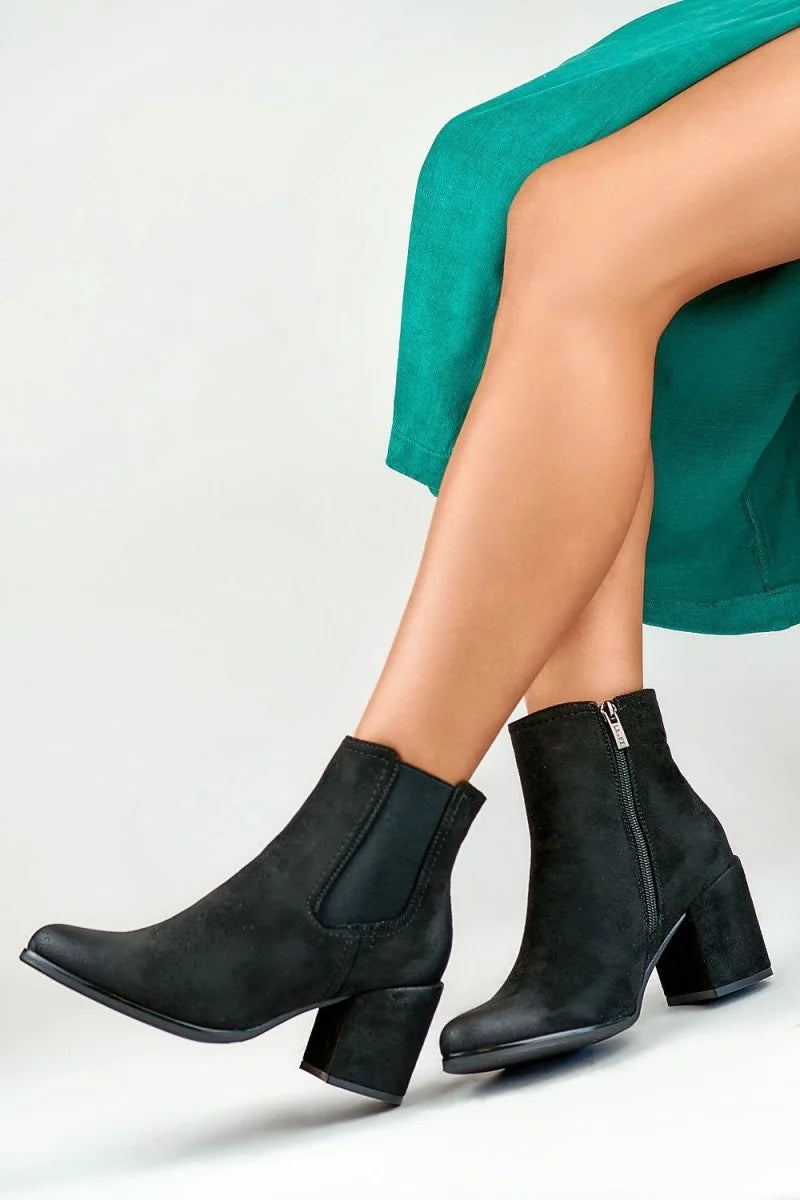 Black suede ankle boots with block heels and side zippers on model.