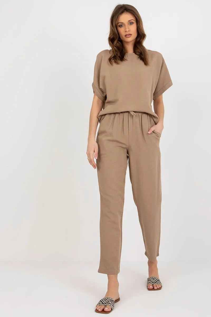 Full-length shot of a woman wearing a light brown cotton blend t-shirt and pants set, with patterned flat sandals.