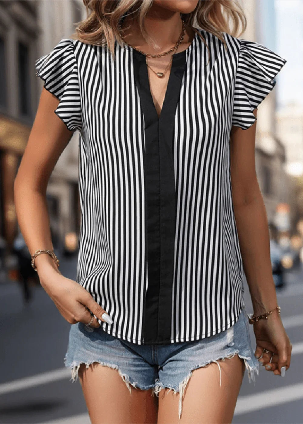 Woman wearing a black and white striped V-neck blouse with ruffled sleeves and denim shorts.