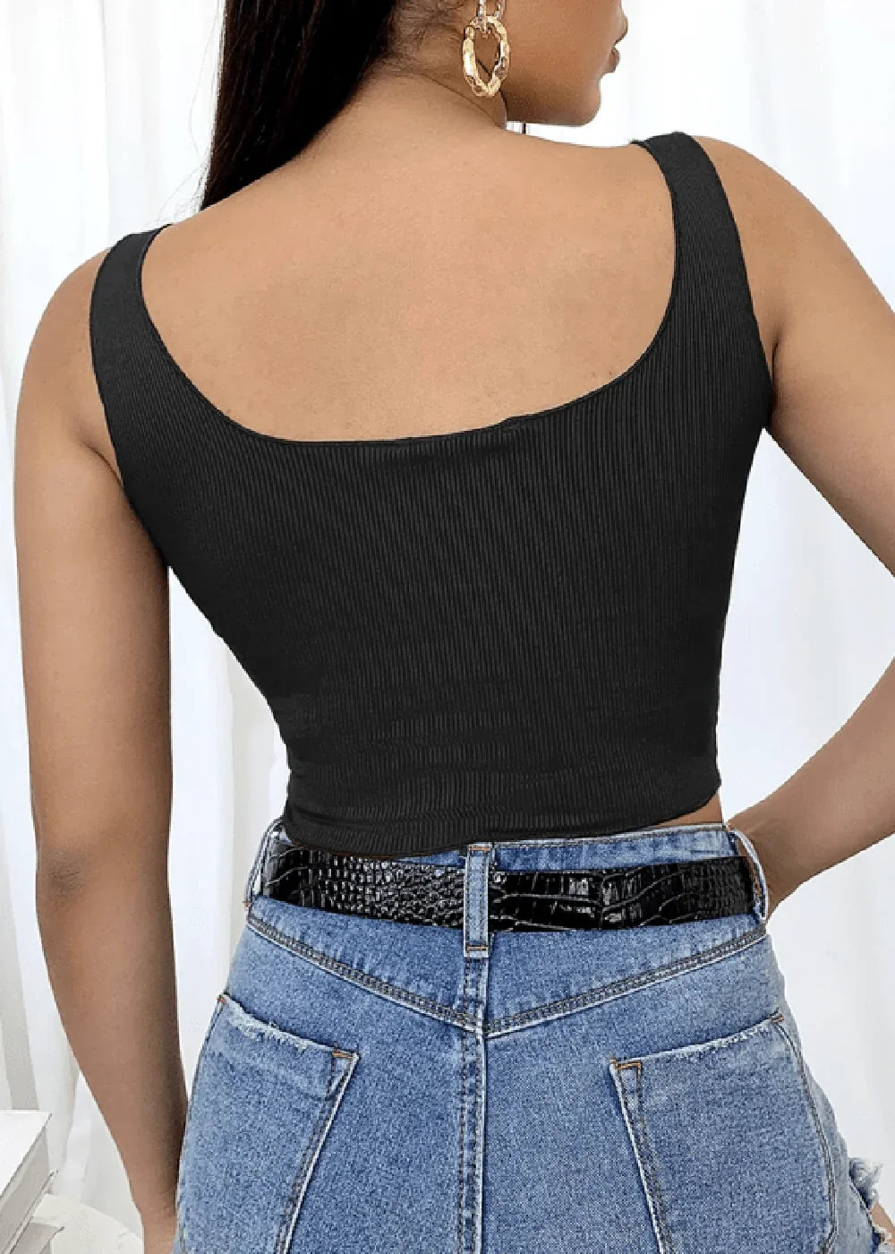 Back view of a black ribbed crop top on a model wearing blue jeans and a black belt.