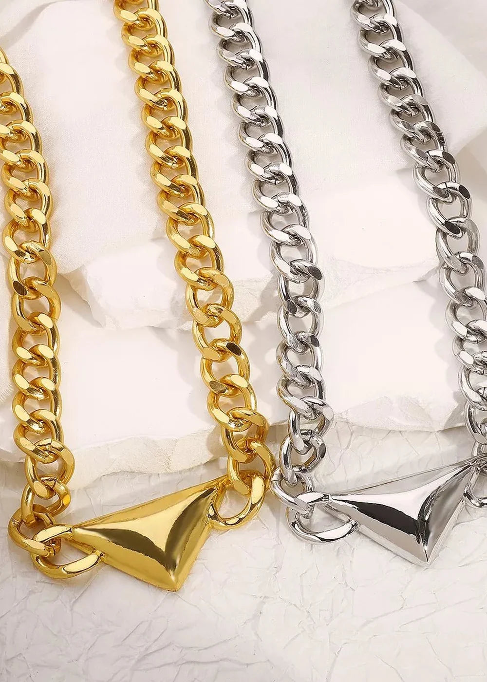 Two chunky chain necklaces, one gold and one silver, with geometric triangular pendants.