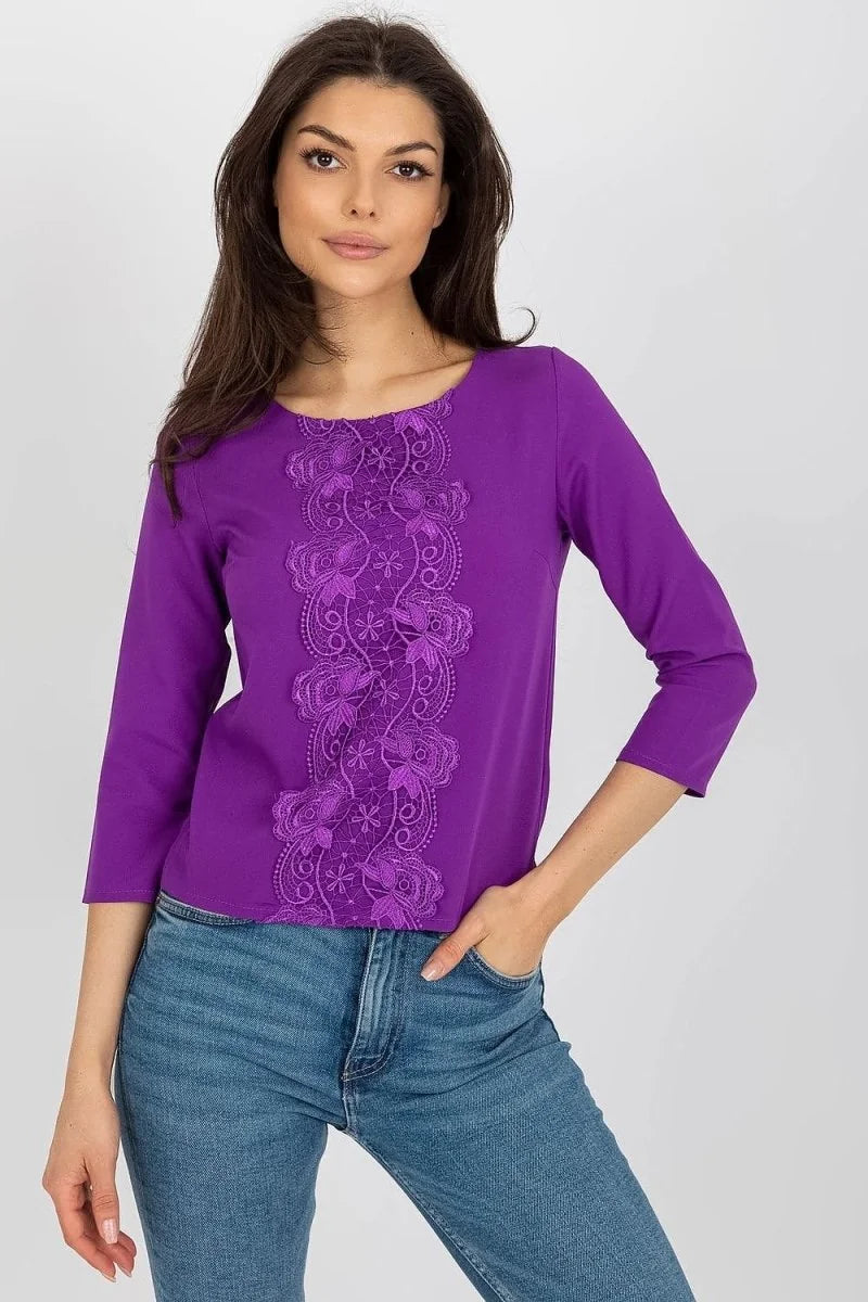 Purple long-sleeve top with intricate lace floral detail down the front, paired with blue jeans on a model.