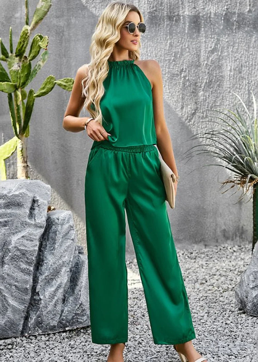Woman in a green satin halter top and wide-leg pants, holding a light-colored clutch.