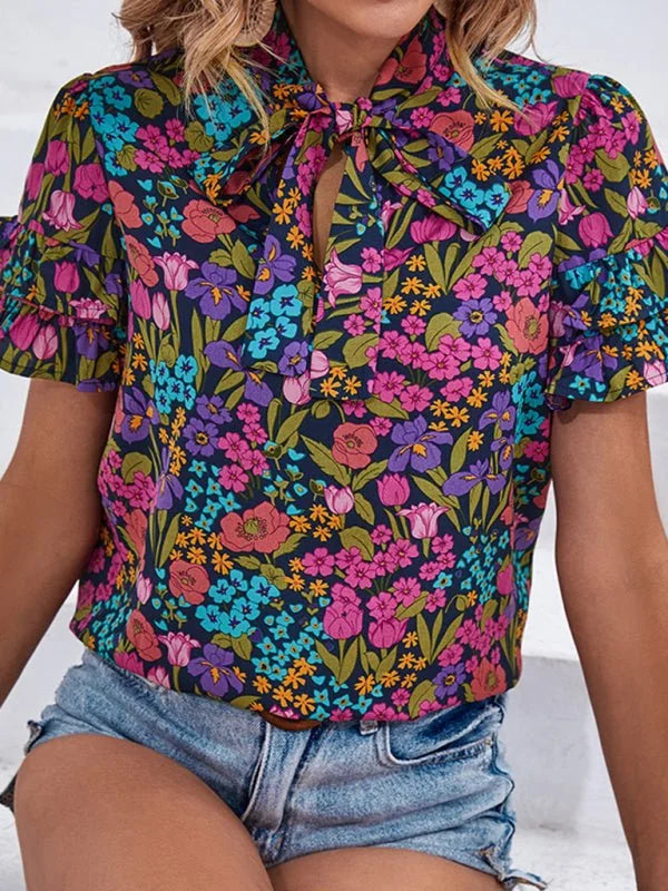 Navy blue top with a vibrant floral print, tie-neck, and ruffled short sleeves.
