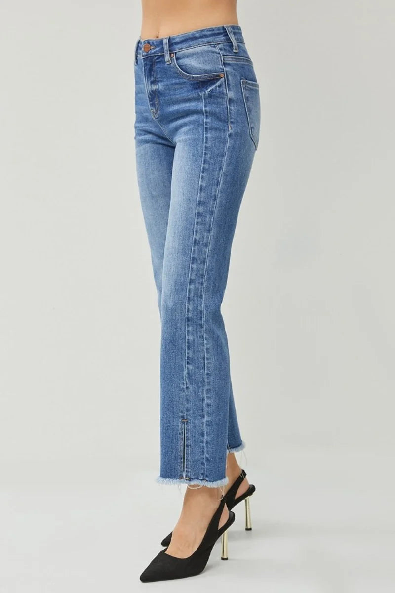 High-waisted blue denim jeans with a frayed hem and ankle slit, on a model wearing black heels.