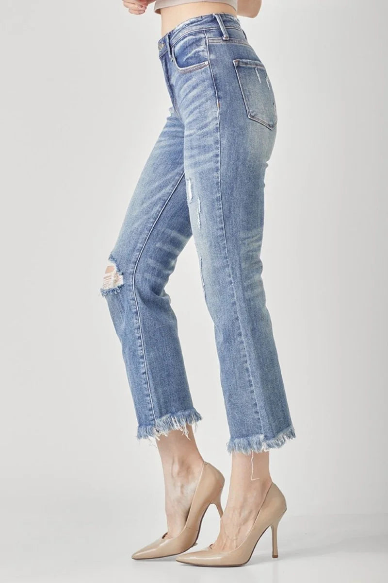 Light wash distressed denim jeans with frayed hem and a ripped knee, shown on model.