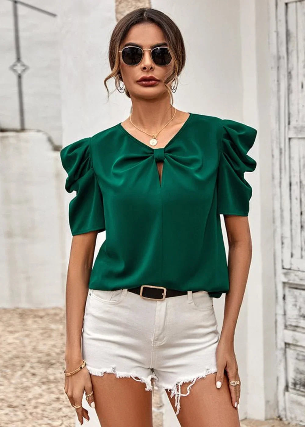 Green satin bow-neck blouse with puff sleeves and white distressed denim shorts on a model.