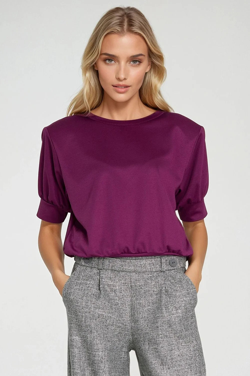 Woman in plum oversized top with puffed sleeves and grey trousers with button detail.