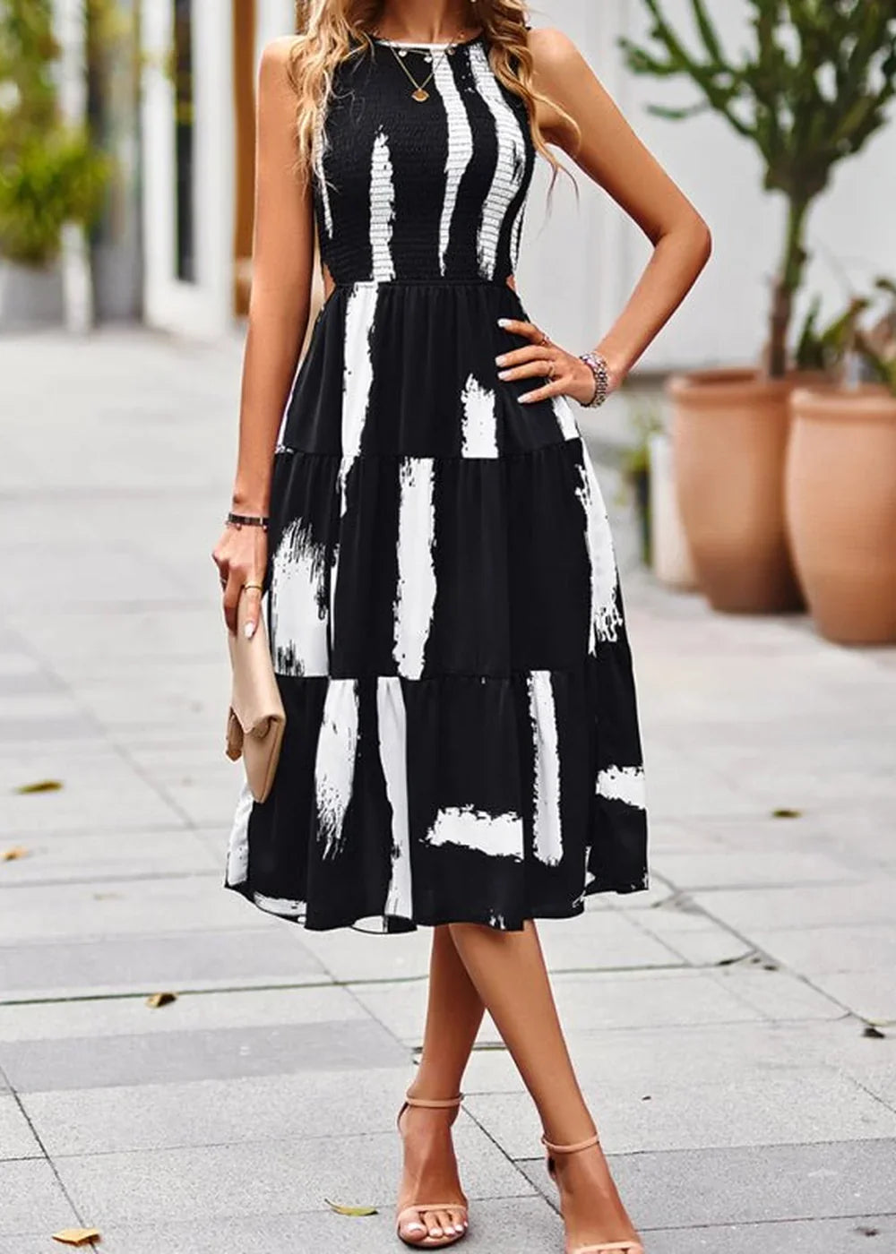 Black and white abstract brushstroke print tiered midi dress with cutout sides and a gold pendant necklace.