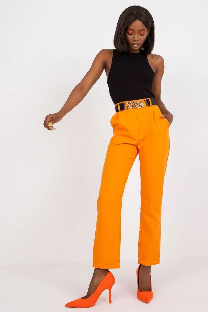 Woman in orange pants with a black and gold chain belt and black tank top.