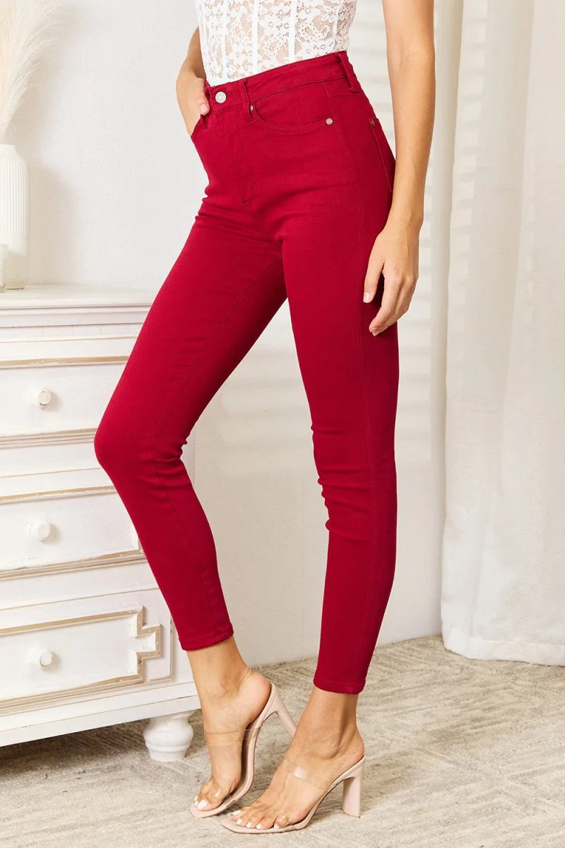 Red high-waisted skinny jeans with a button closure, shown on a model wearing clear strap heels.